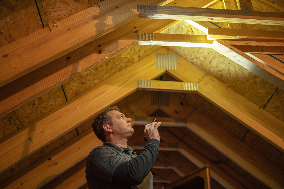 A man inspecting an attic with a flashlight.