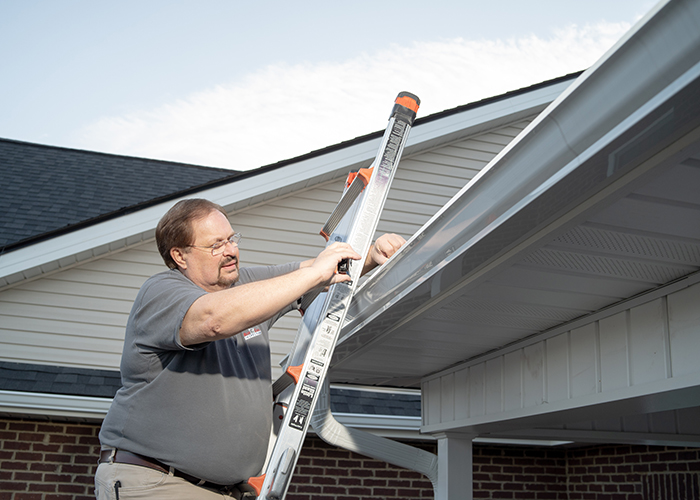 Home Inspector Gene on a ladder taking photos of a section of a roof.