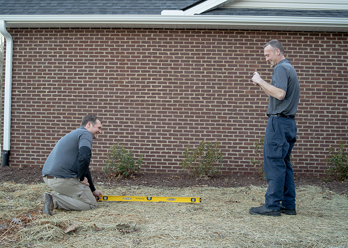 Jon and Tanner inspecting the foundation of a brick house.