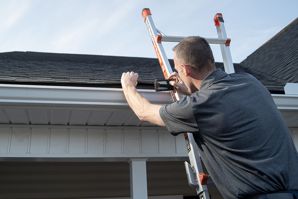 InterNACHI certified Home Inspector Tanner on a ladder taking photos of a roof.